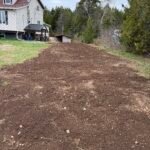 Gravel walkway installation in progress with compact excavator and tools at a residential property in New Brunswick.